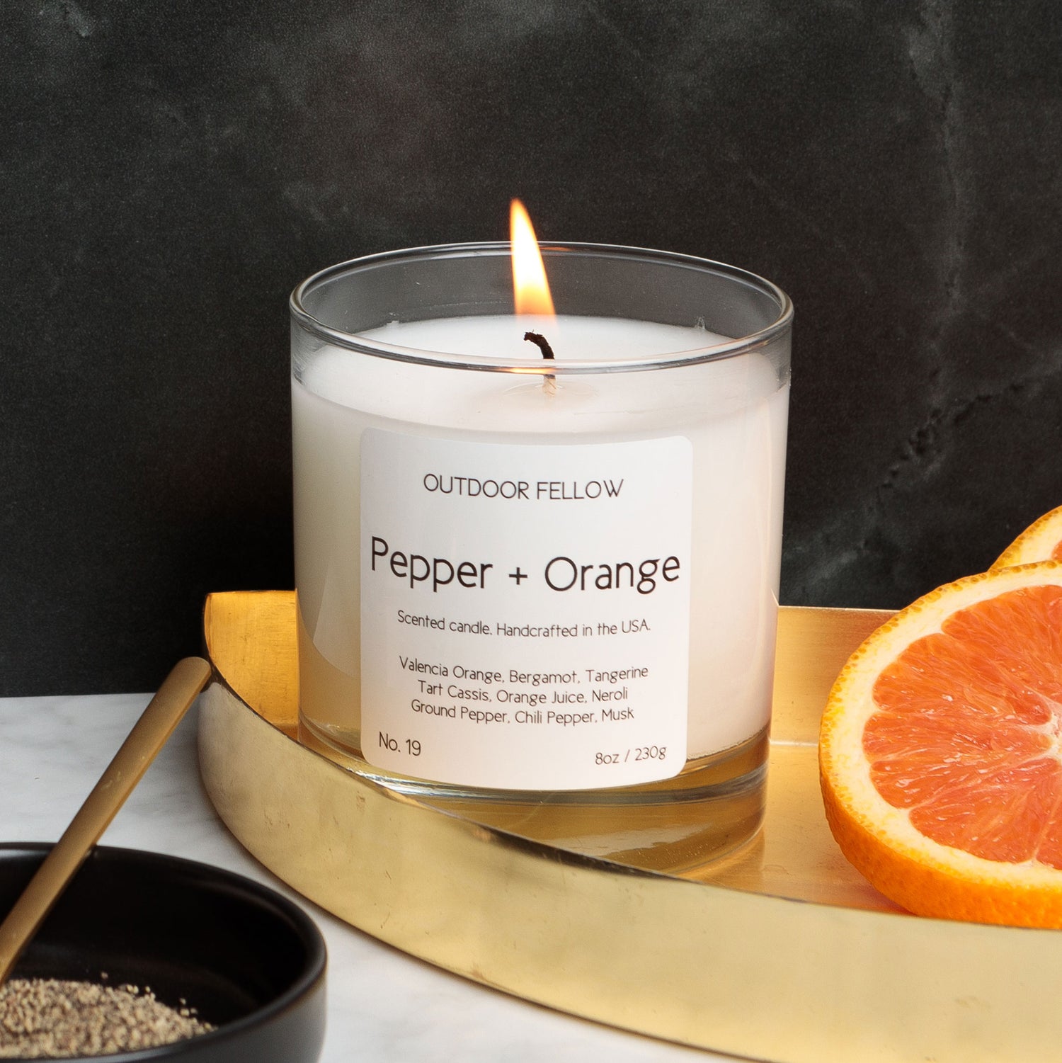 Pepper and Orange scented candle on a gold tray next to orange slices and ground pepper