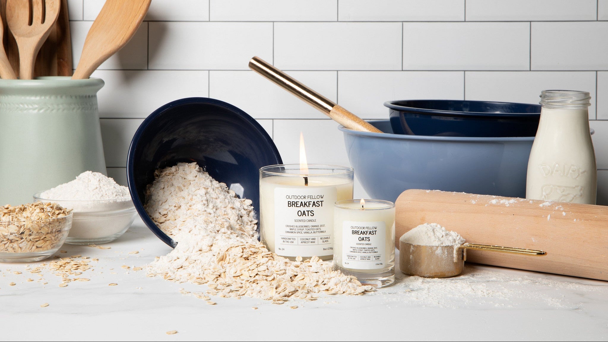 Candles labeled 'Breakfast Oats' on a kitchen counter with oats, flour, and kitchen utensils.
