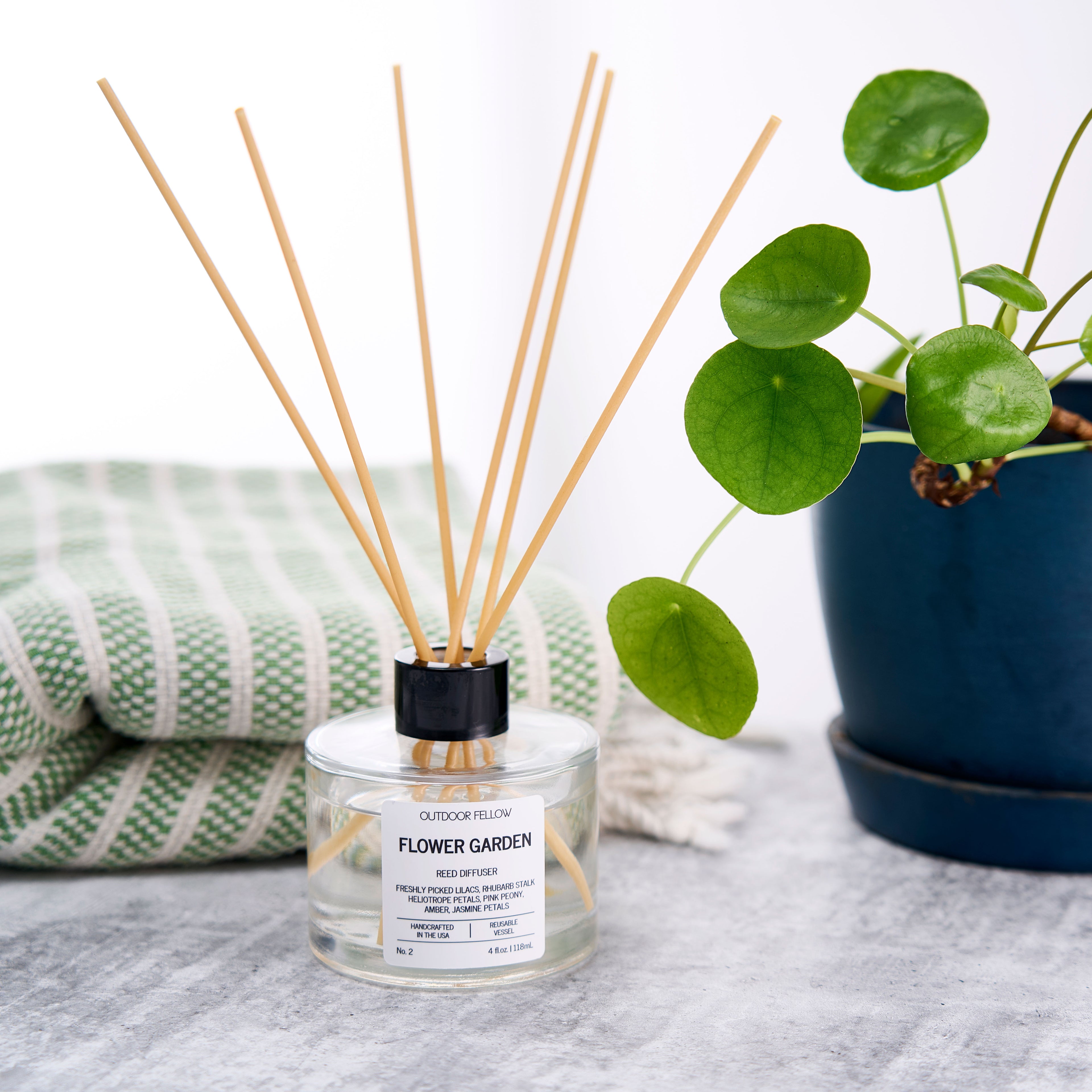 Flower Garden reed diffusers on a concrete surface next to a plant and towel