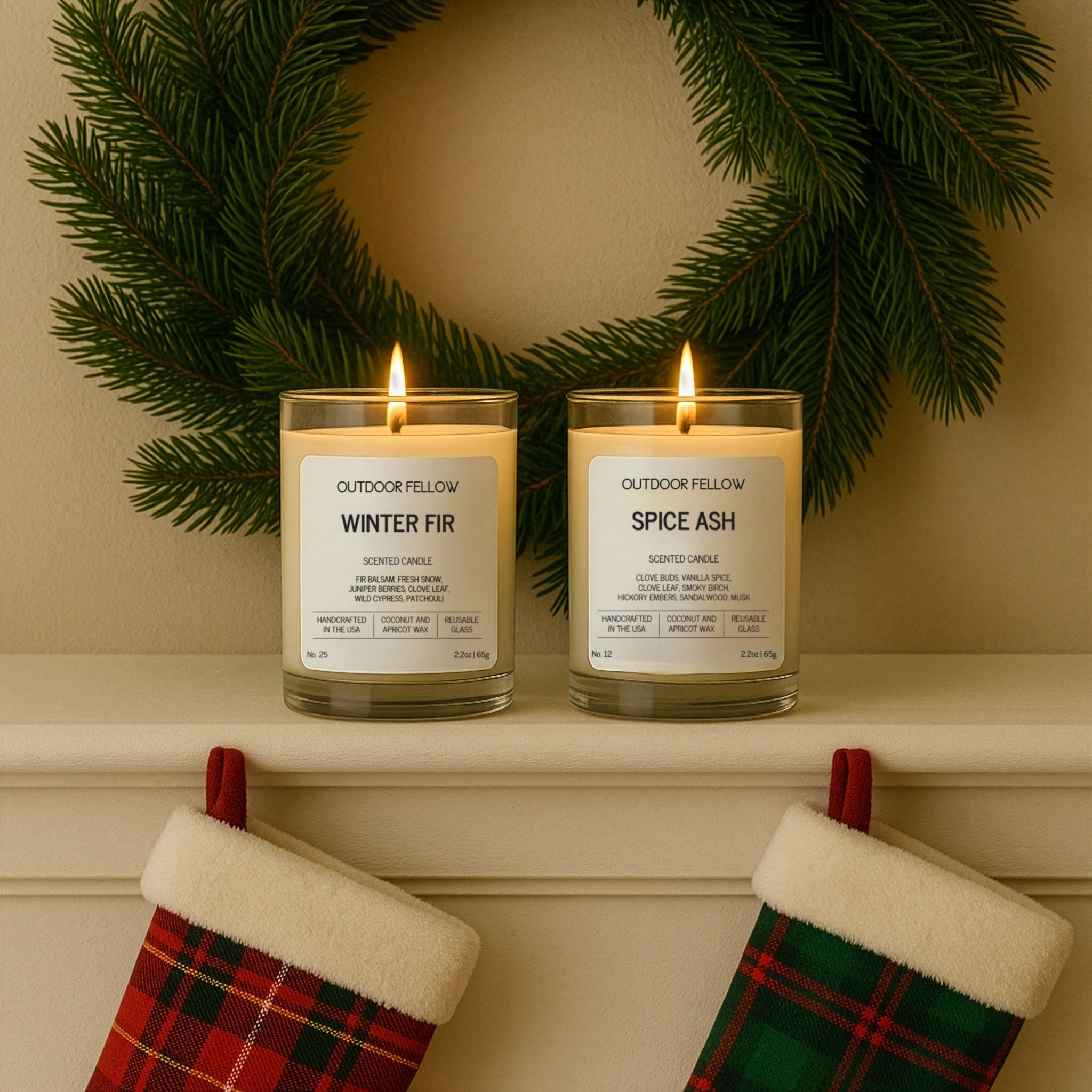 Two lit Outdoor Fellow Winter Fir and Spice Ash mini candles sit on a holiday mantle beneath a green wreath, with plaid red and green stockings hanging below for a festive touch.