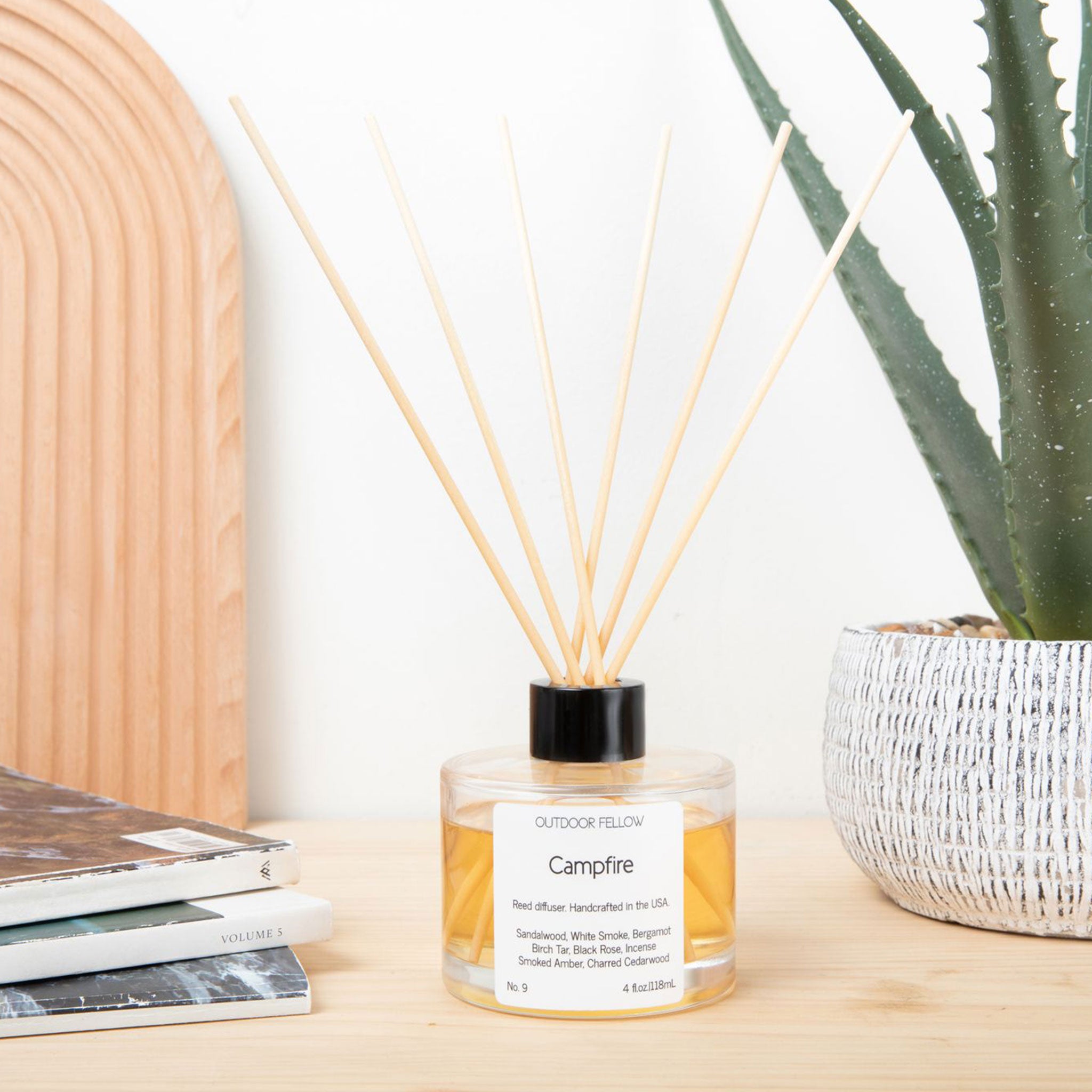 Campfire reed diffuser next to magazines and a potted agave plant
