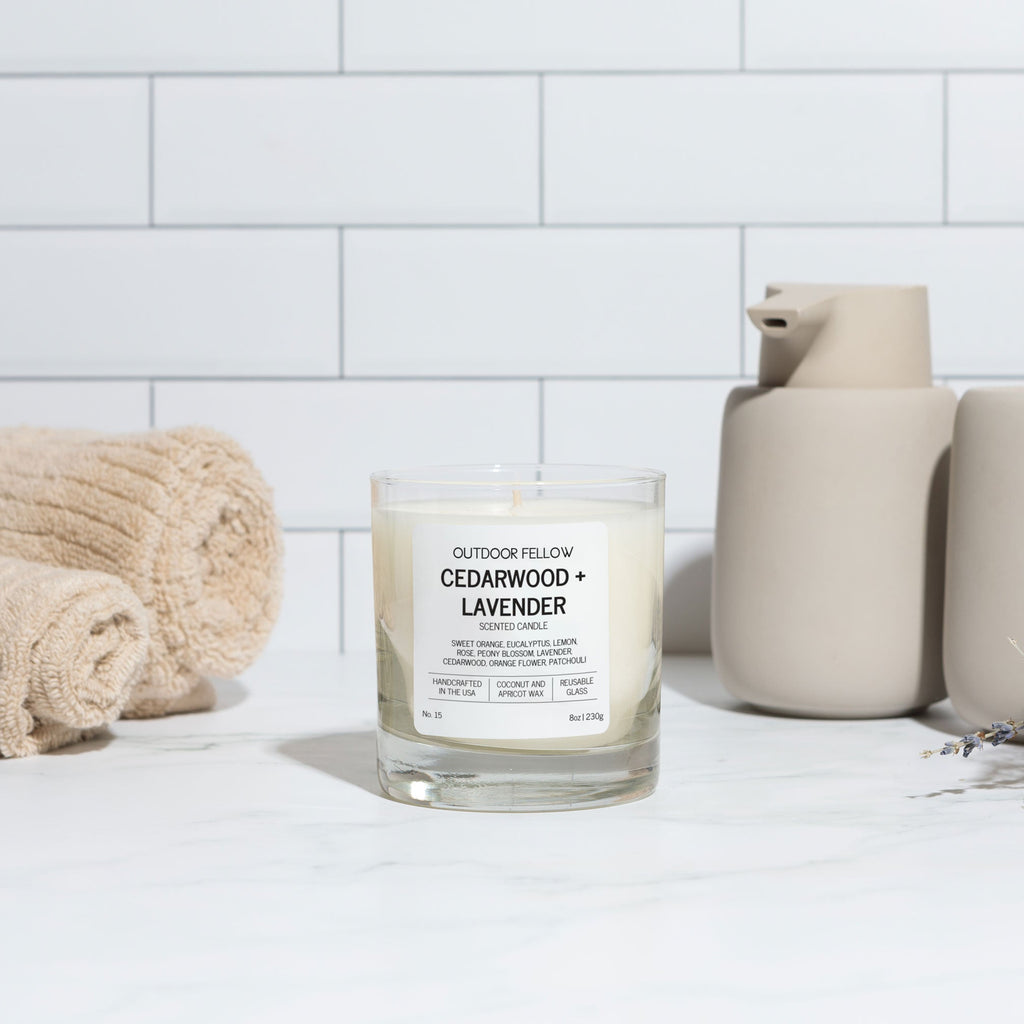 Candle labeled 'Cedarwood + Lavender' on a white surface with a tiled wall background