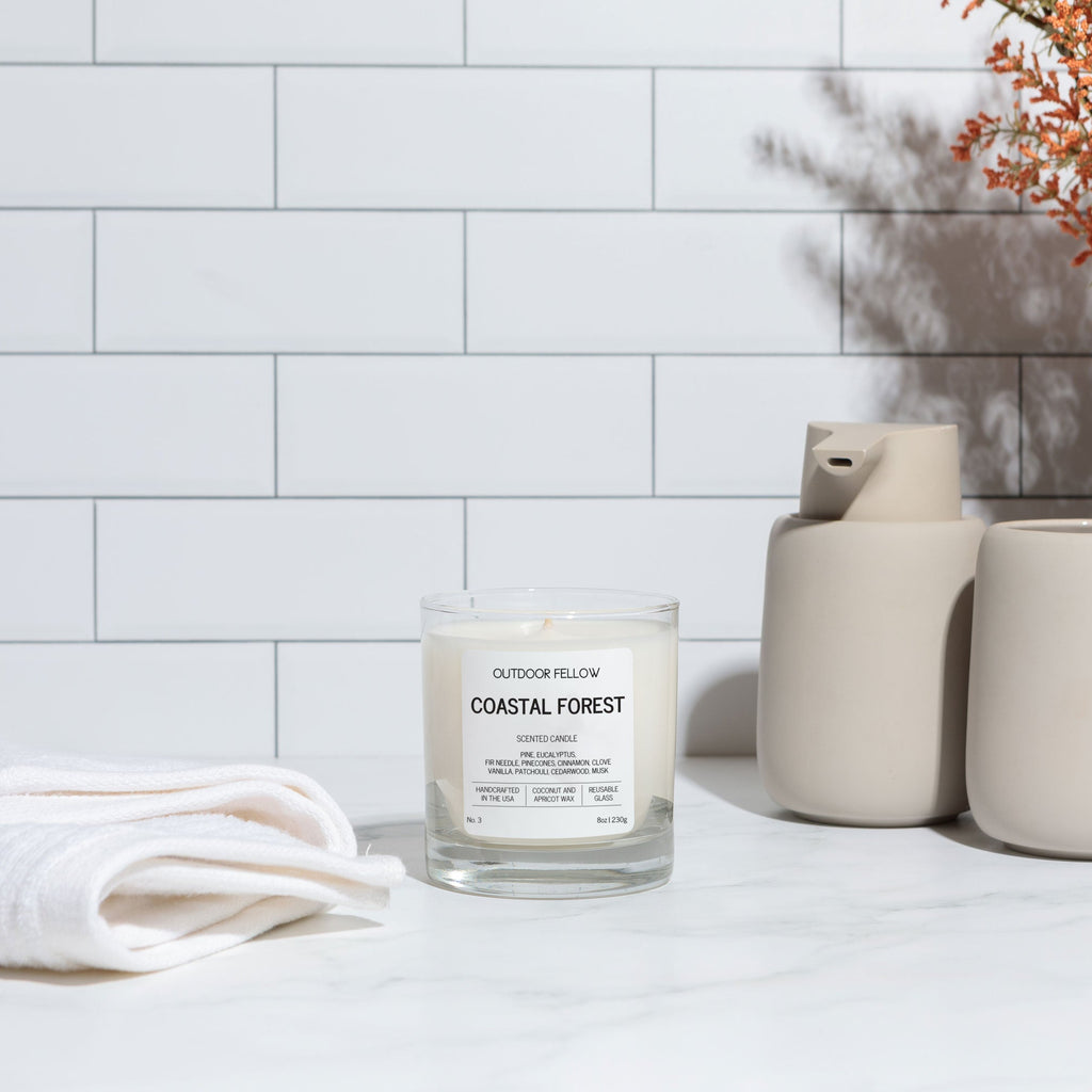 Candle labeled 'Coastal Forest' on a white surface with decorative items and a tiled wall background