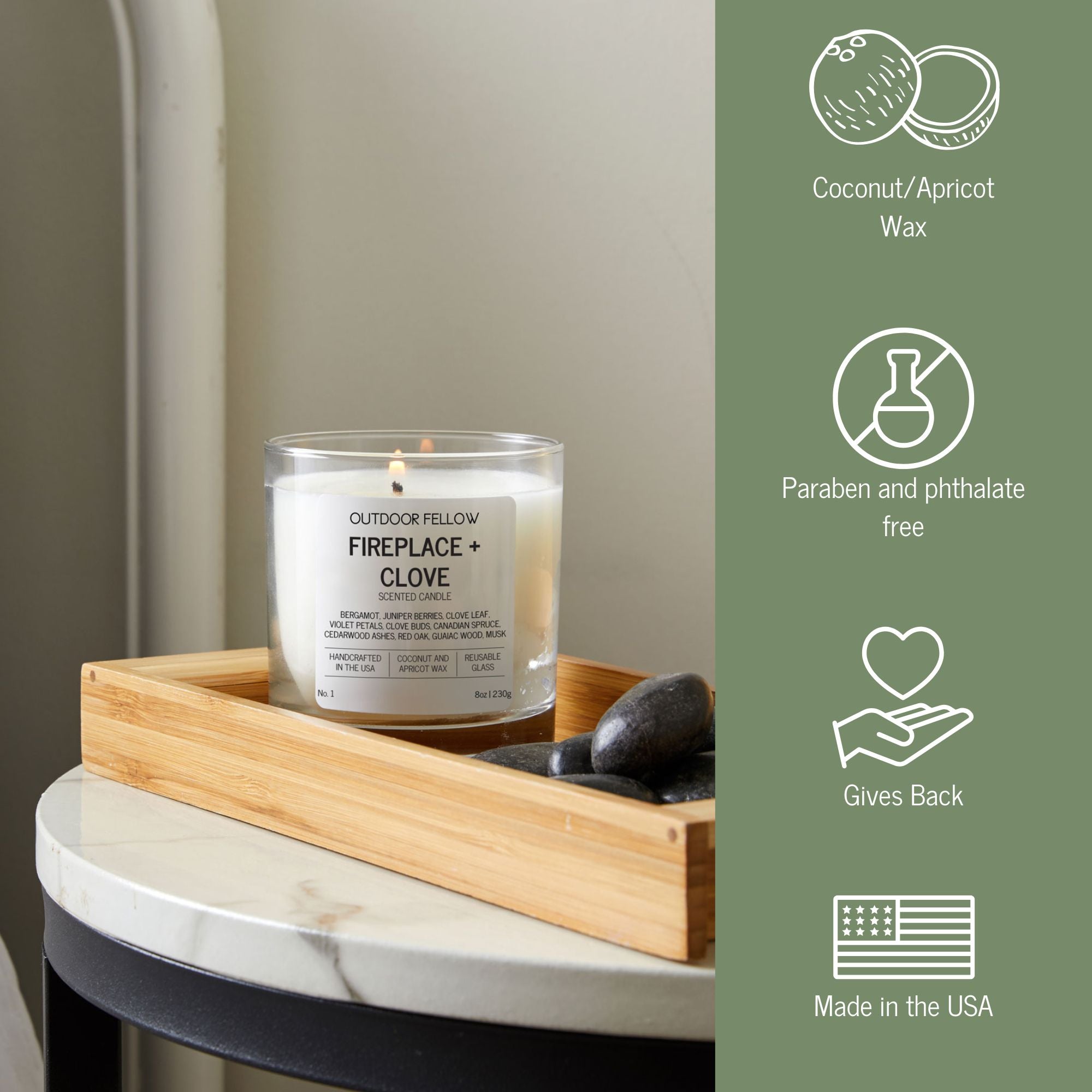 Fireplace + Clove candle in a glass jar on a wooden tray with stones, next to icons highlighting features: coconut/apricot wax, paraben and phthalate free, gives back, and made in the USA.
