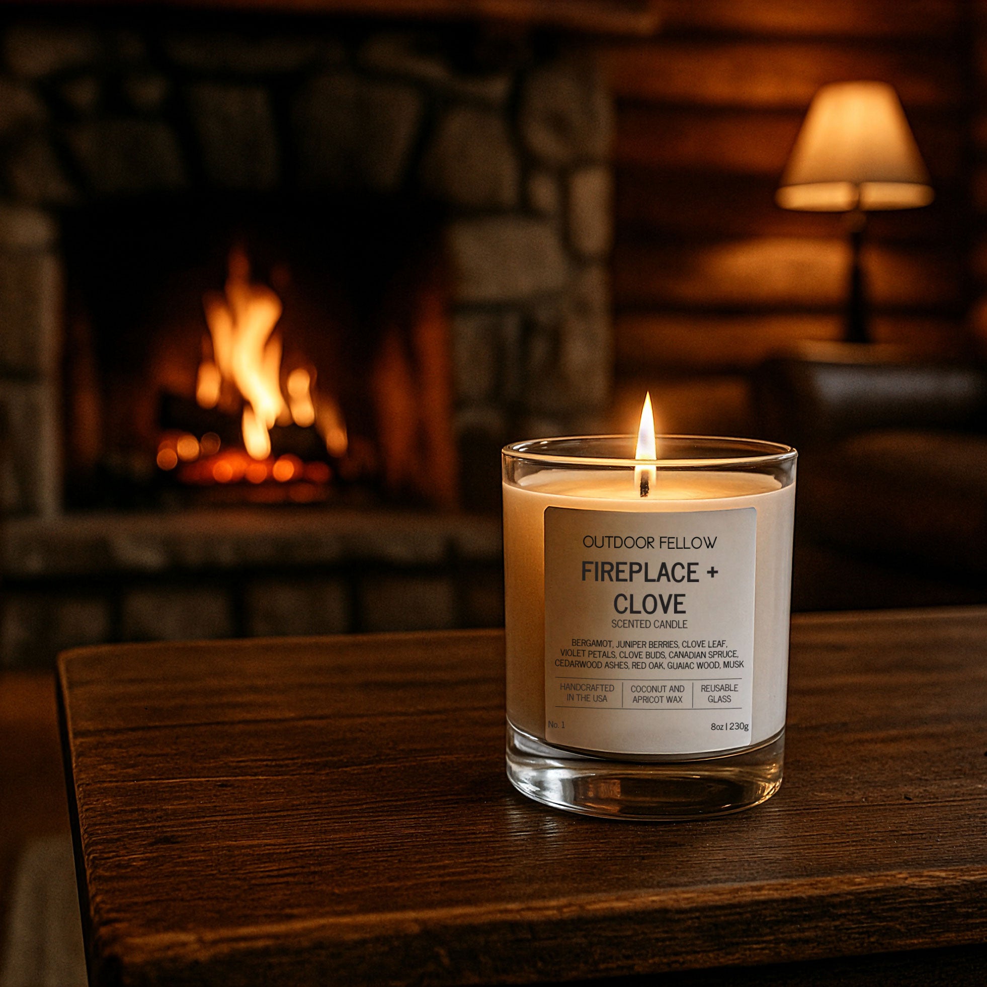 Candle labeled 'Fireplace + Clove' on a wooden surface with a fireplace in the background