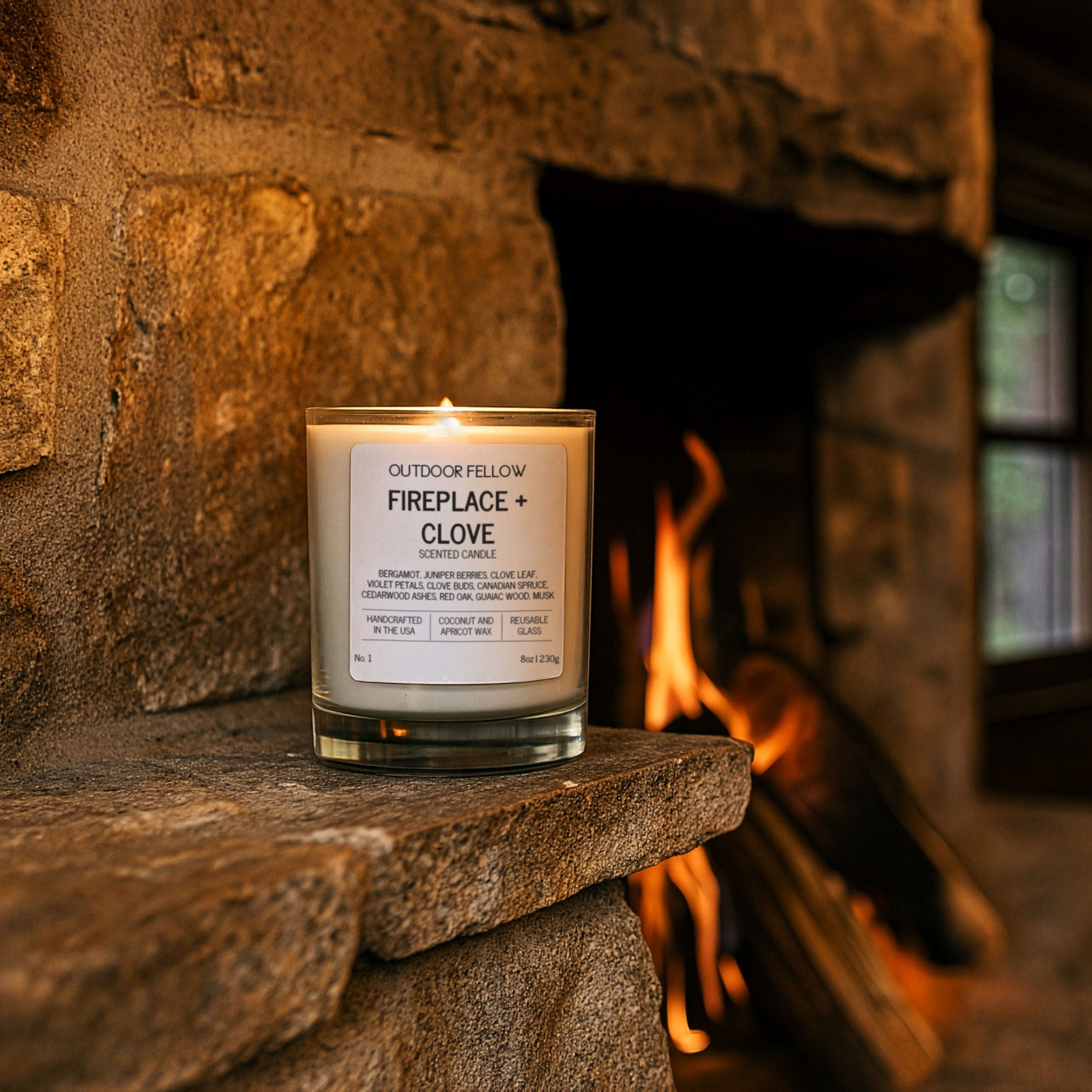 Candle labeled 'Fireplace + Clove' on a stone fireplace mantle with flames in the background