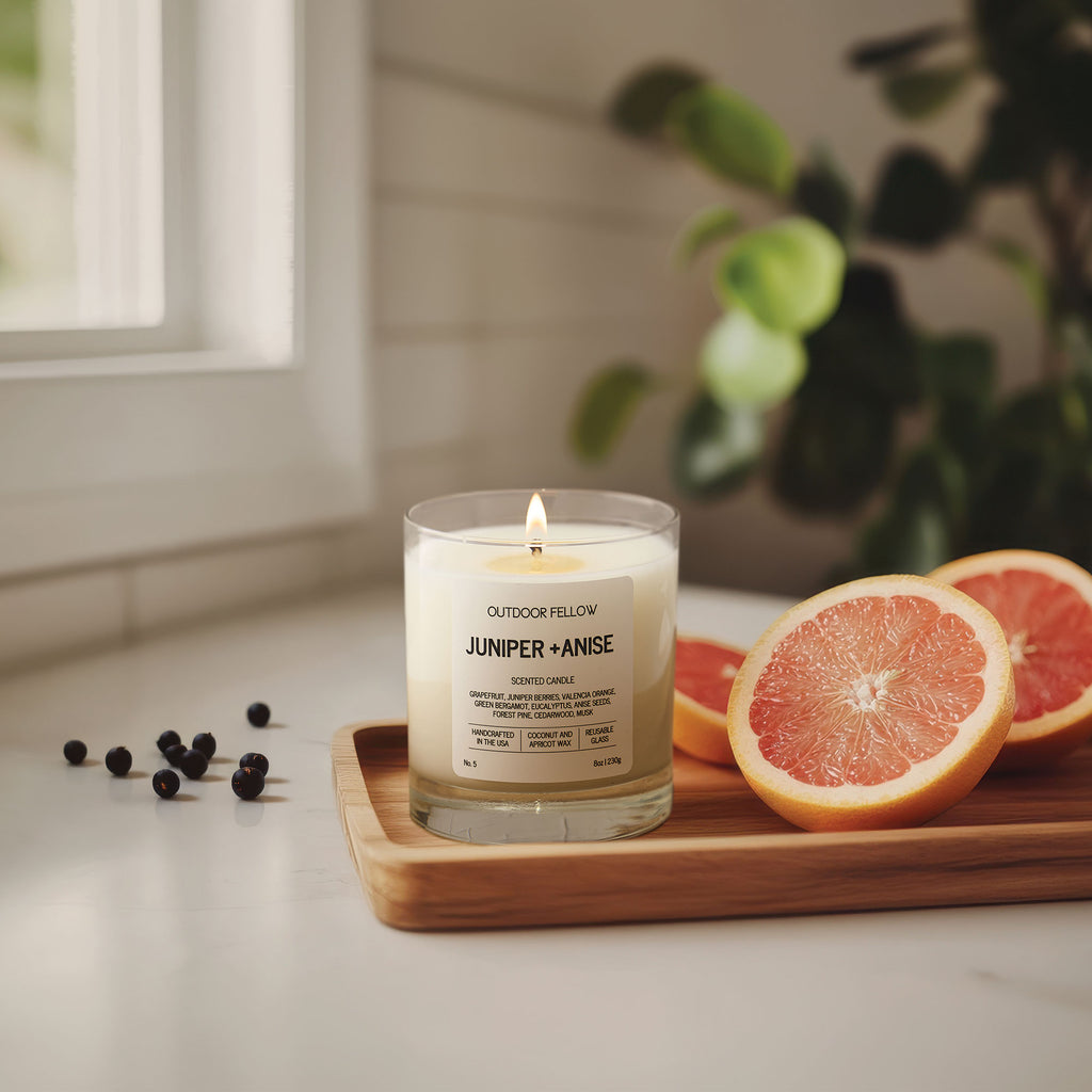 Juniper and Anise scented candle on a wooden tray next to cut grapefruits a brightly lit room