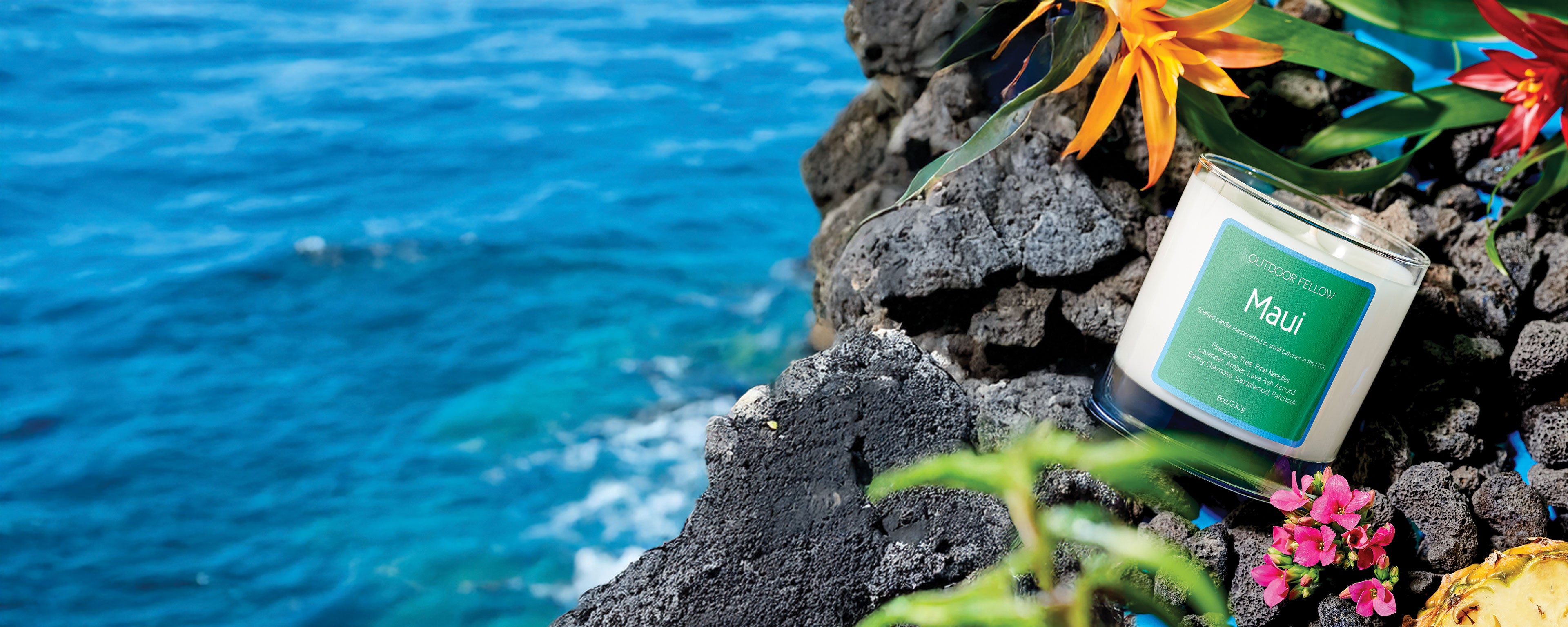 Maui scented candle on lava rocks surrounded by flowers next to the ocean