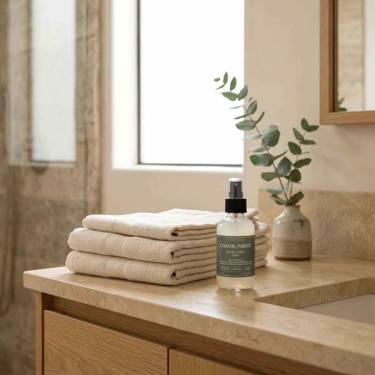 Outdoor Fellow Coastal Forest Room & Linen Spray styled on a bathroom vanity beside folded linen towels and eucalyptus.