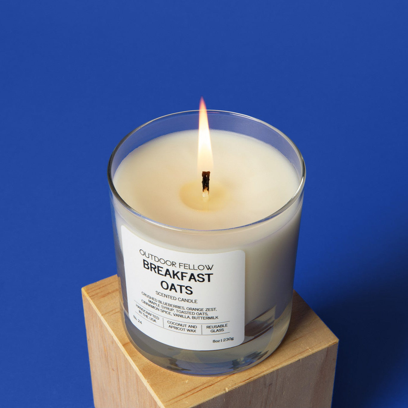 Candle labeled 'Breakfast Oats' on a wooden block with a blue background