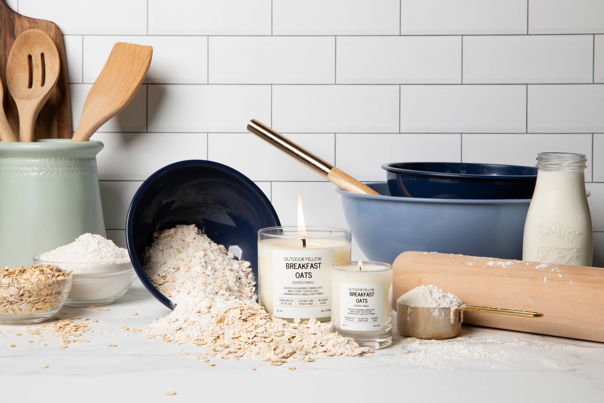 Candles labeled 'Breakfast Oats' on a kitchen counter with oats, flour, and kitchen utensils.
