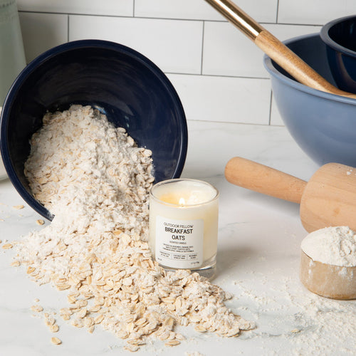 Breakfast Oats mini candle and kitchen utensils on a light surface surrounded by oats with a tiled wall background