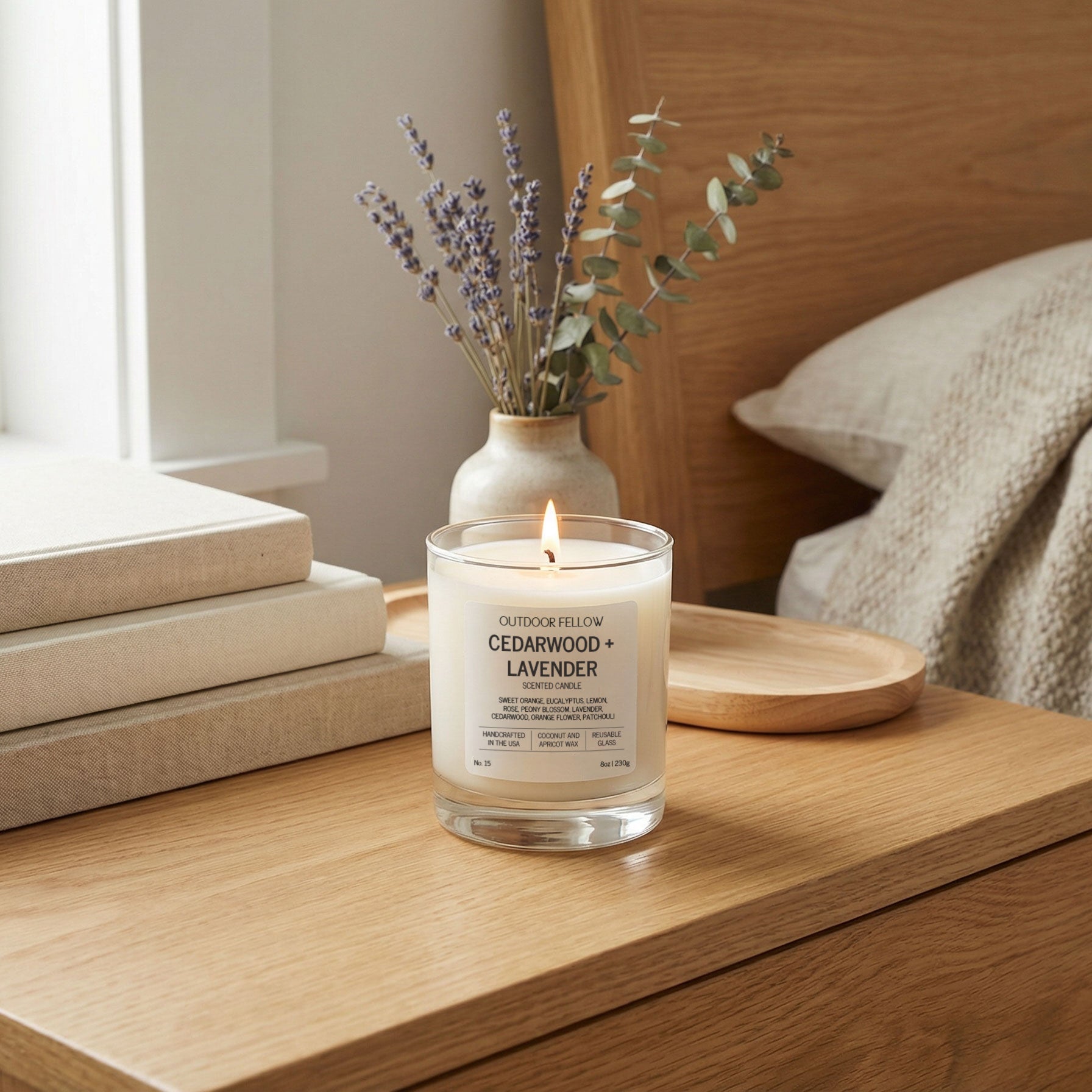 Candle with a wooden holder on a surface next to a vase with lavender and eucalyptus leaves.