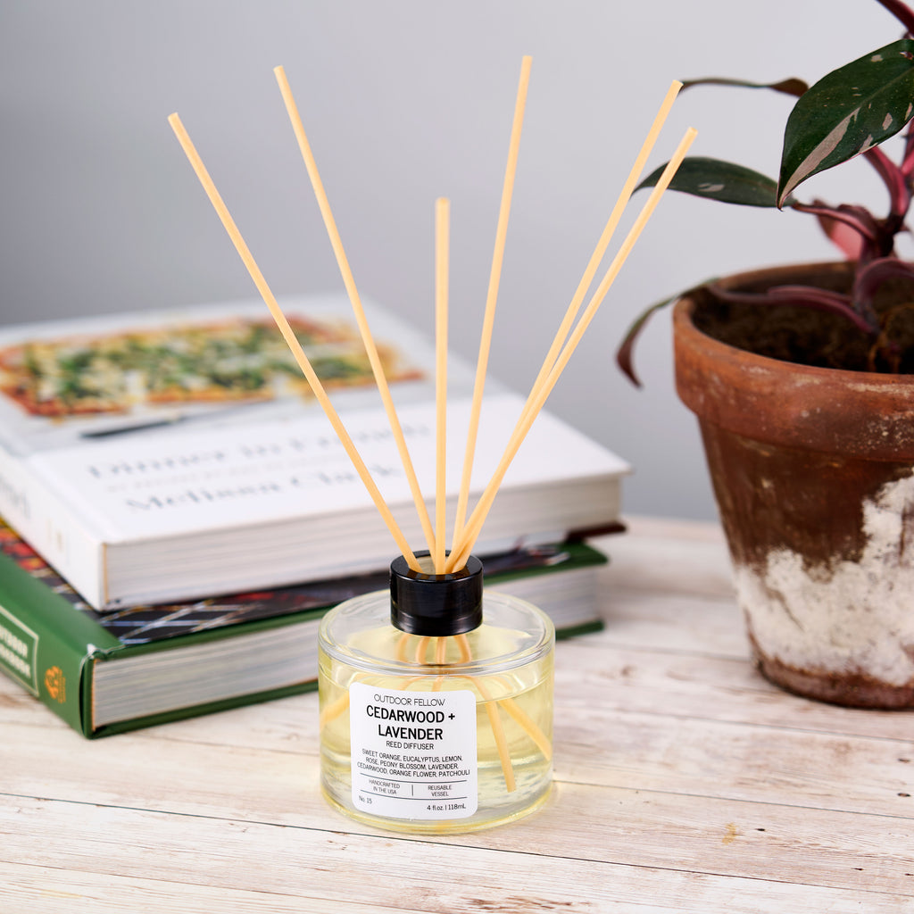 Cedarwood and Lavender reed diffuser on a wooden desk in front of books and a potted plant. 