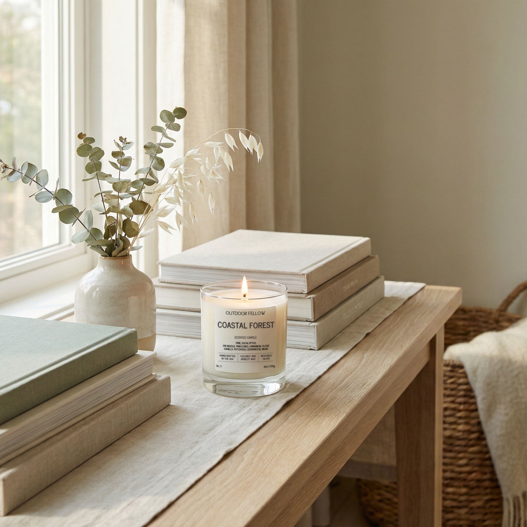 Coastal Forest candle on a wooden table with books and a vase in a bright room