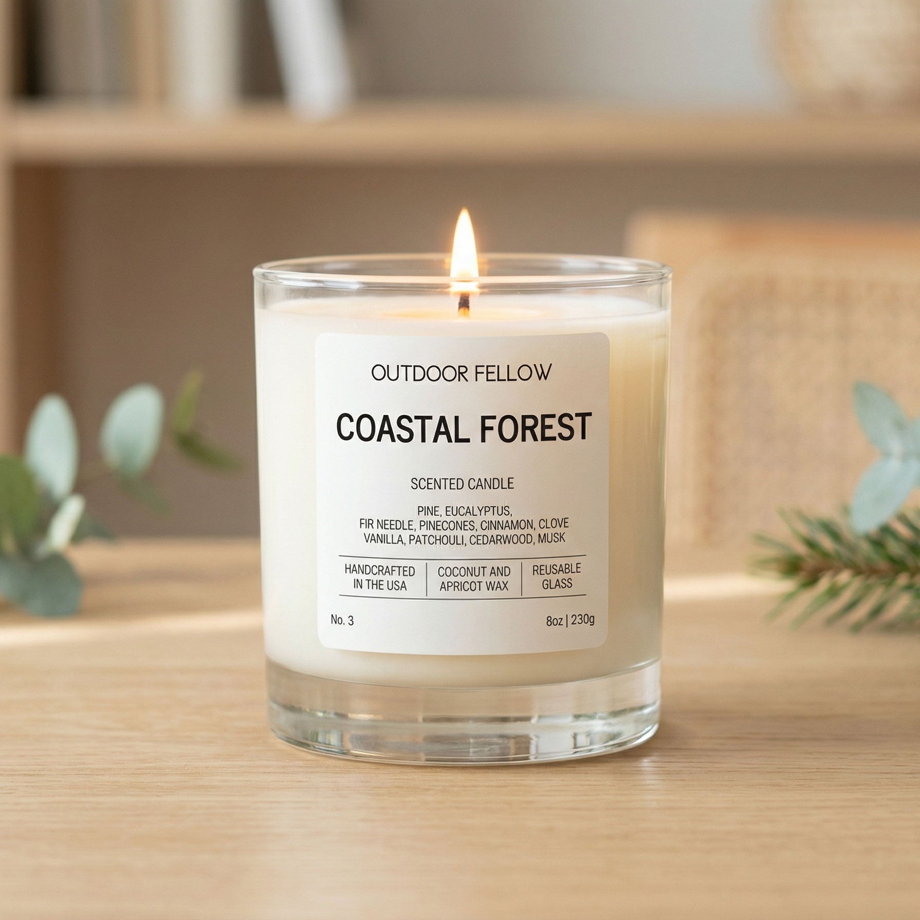 Candle labeled 'Coastal Forest' by 'Outdoor Fellow' on a wooden surface with plants in the background.