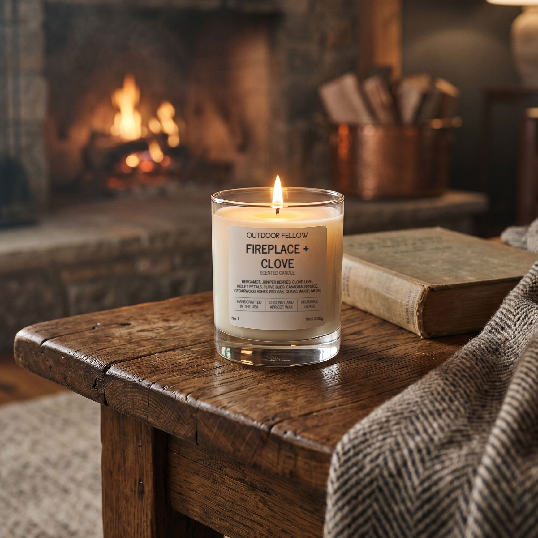 Candle in a glass jar labeled 'Fireplace + Clove' on a wooden table with a fireplace in the background.