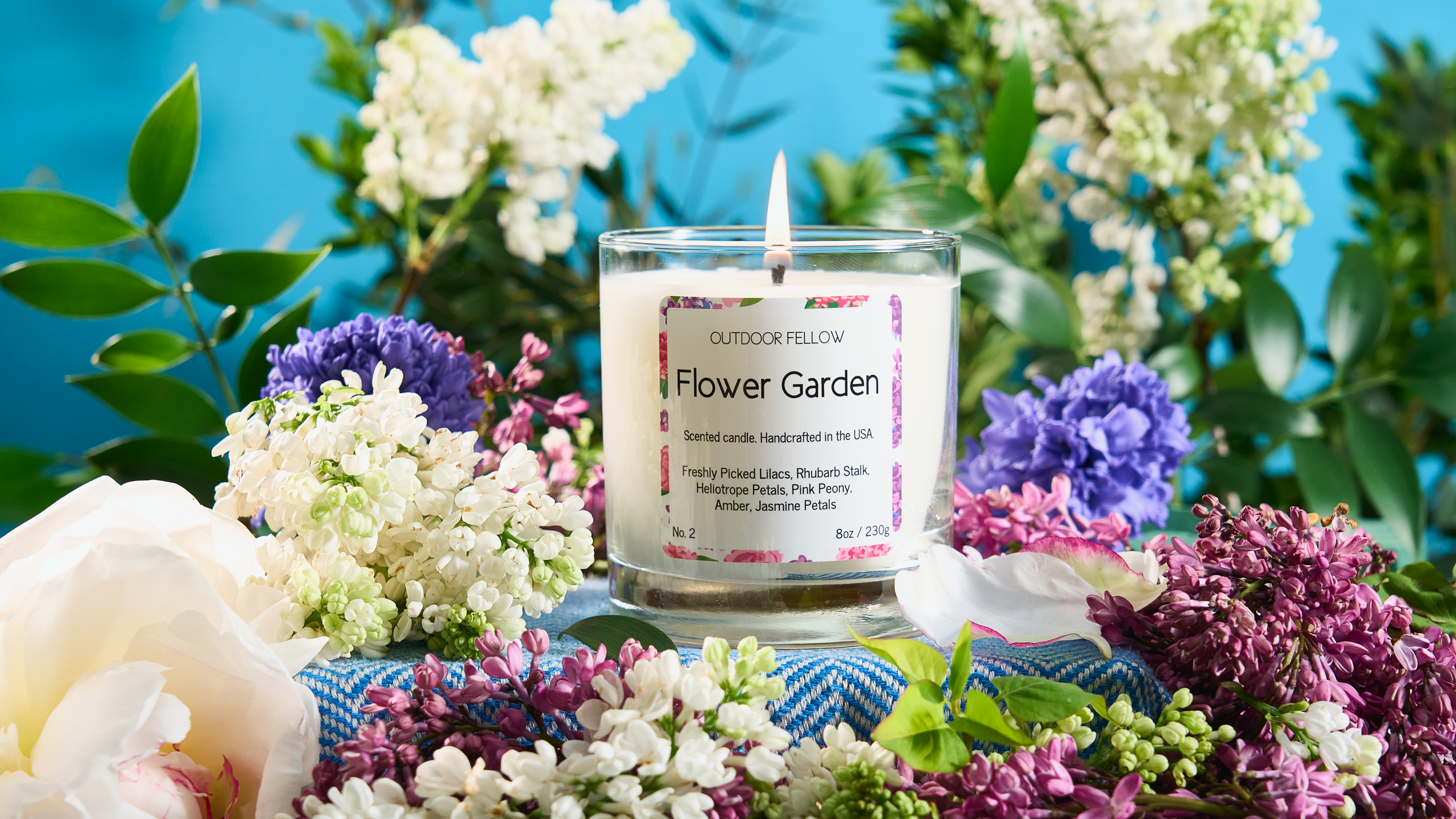 Flower Garden scented candle surrounded by lilacs, peony and other assorted flowers