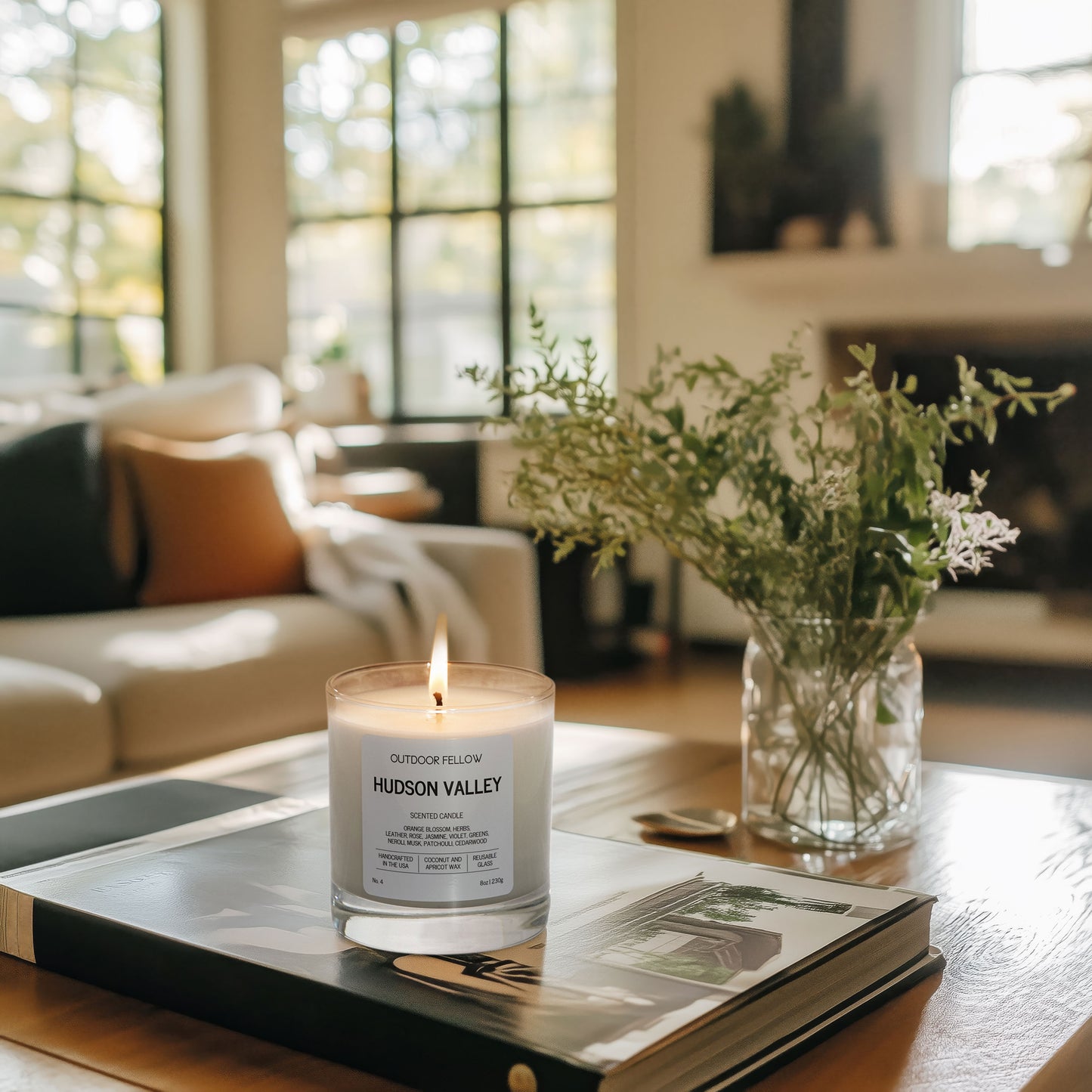 Hudson Valley scented candle on a living room table next to a vase of jasmine