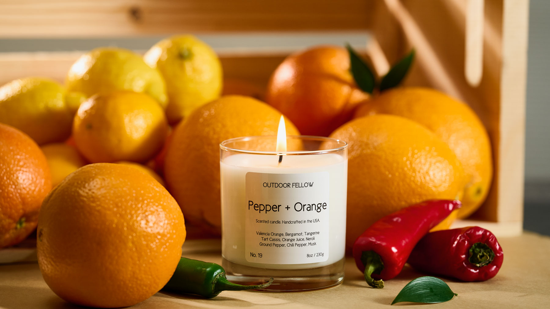 Pepper and Orange scented candle surrounded by oranges and peppers