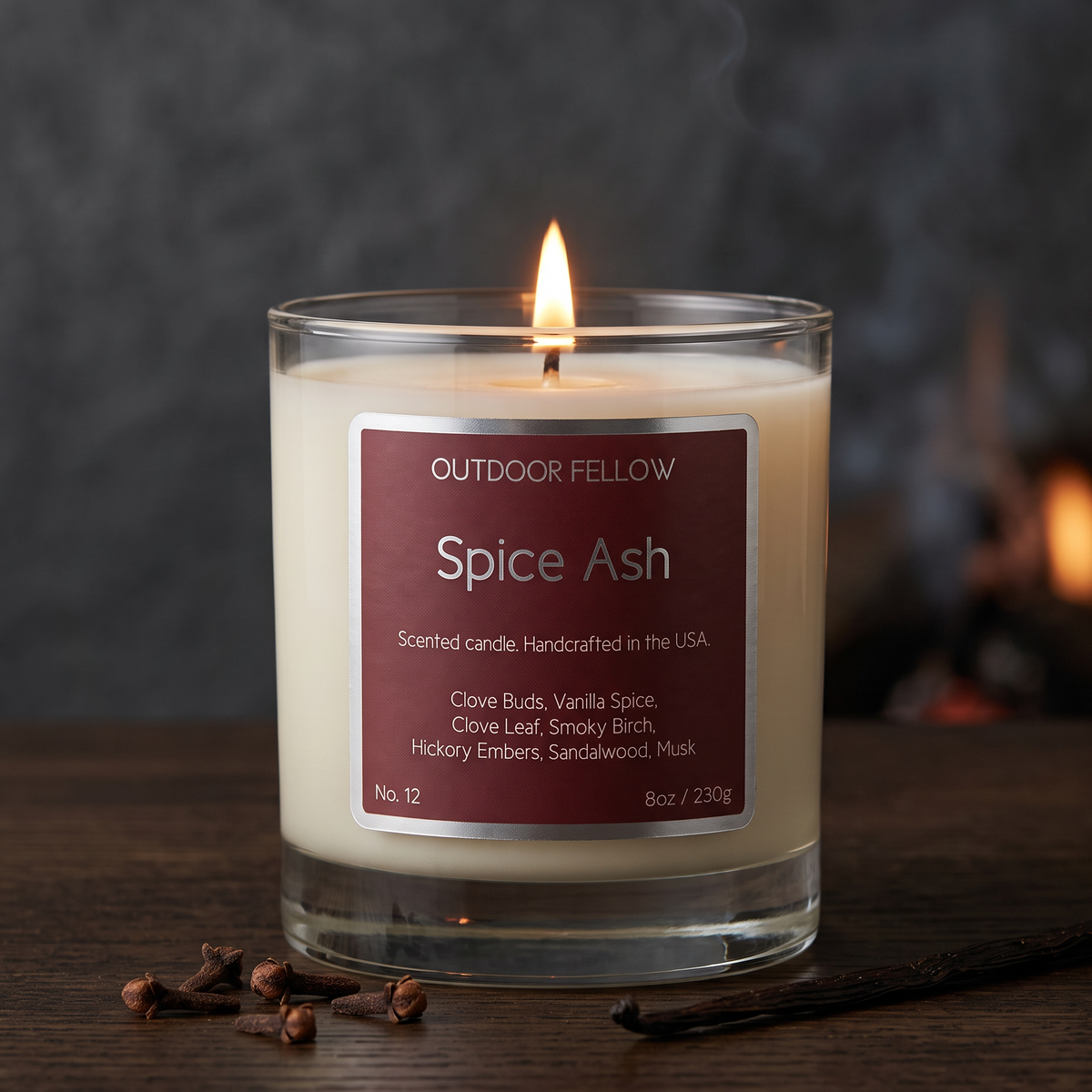 Lit Outdoor Fellow Spice Ash candle on a wooden surface, styled with cloves and vanilla beans against a warm, softly blurred background.