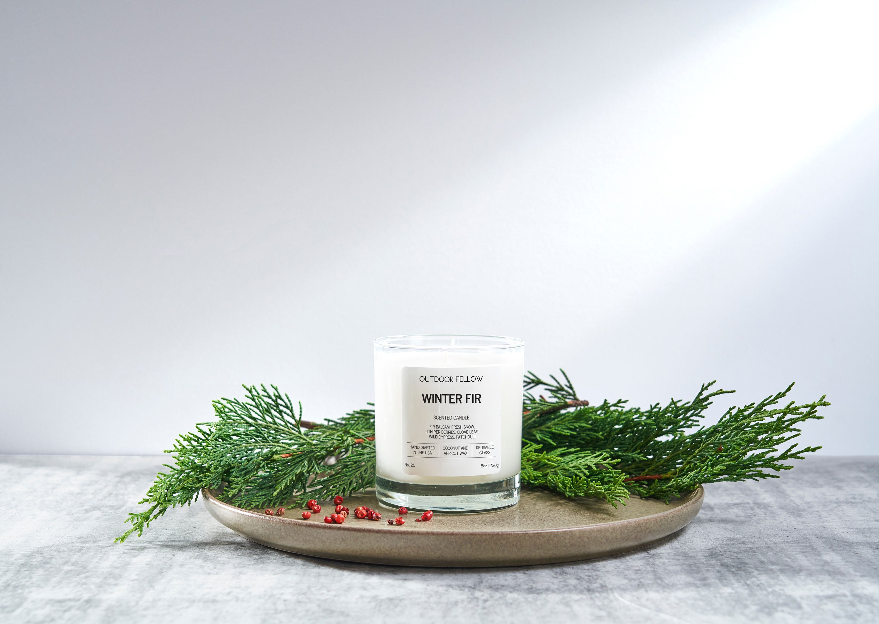 Candle labeled 'Winter Fir' on a decorative plate with greenery on a light background