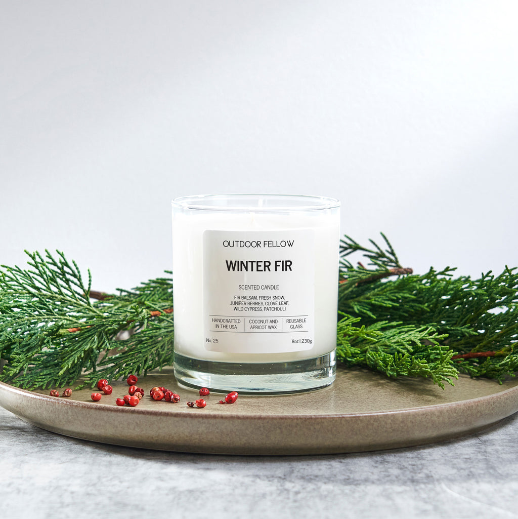 Candle labeled 'Winter Fir' by Outdoor Fellow on a plate with greenery
