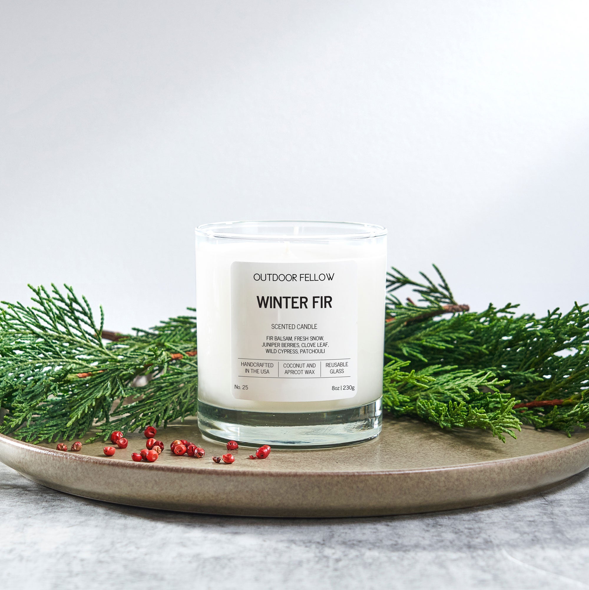 Candle labeled 'Winter Fir' by Outdoor Fellow on a plate with greenery