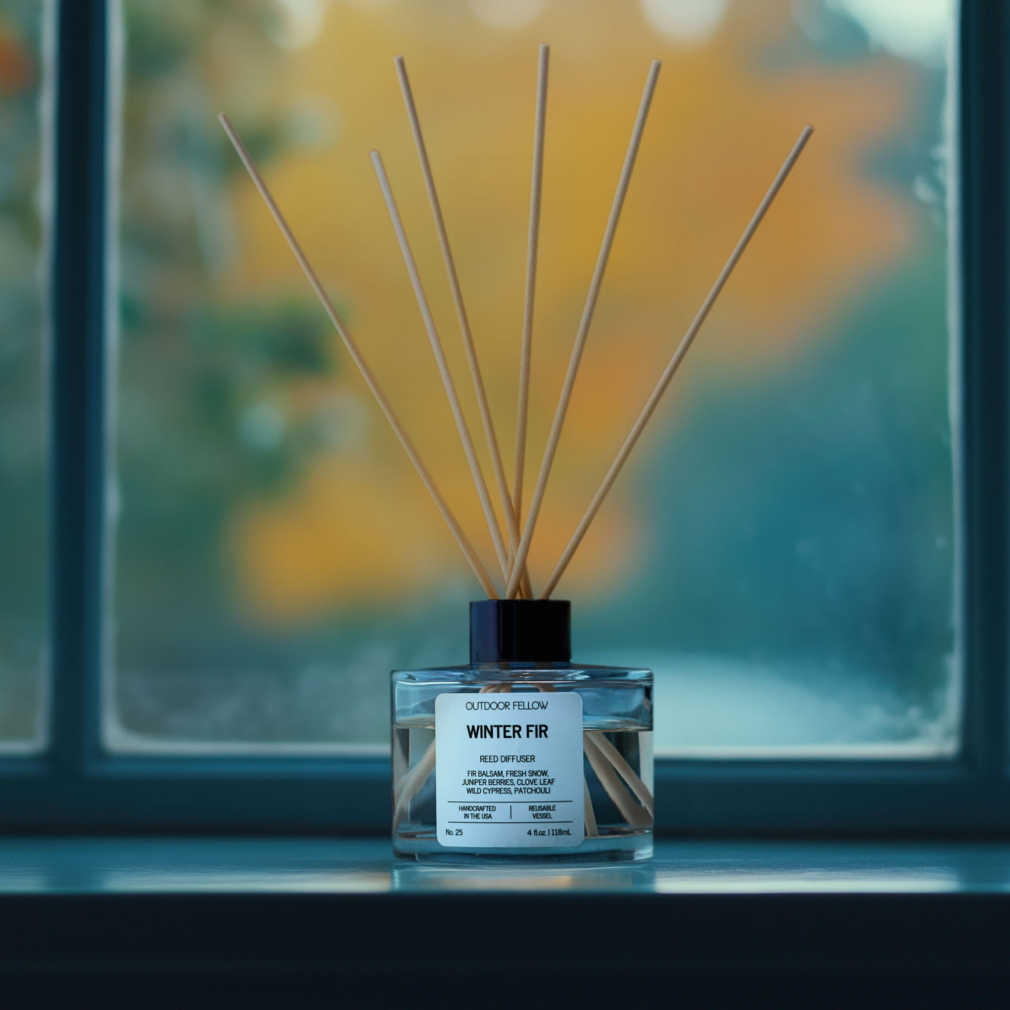 Winter Fir reed diffuser on a window sill in front of a window with frost on it