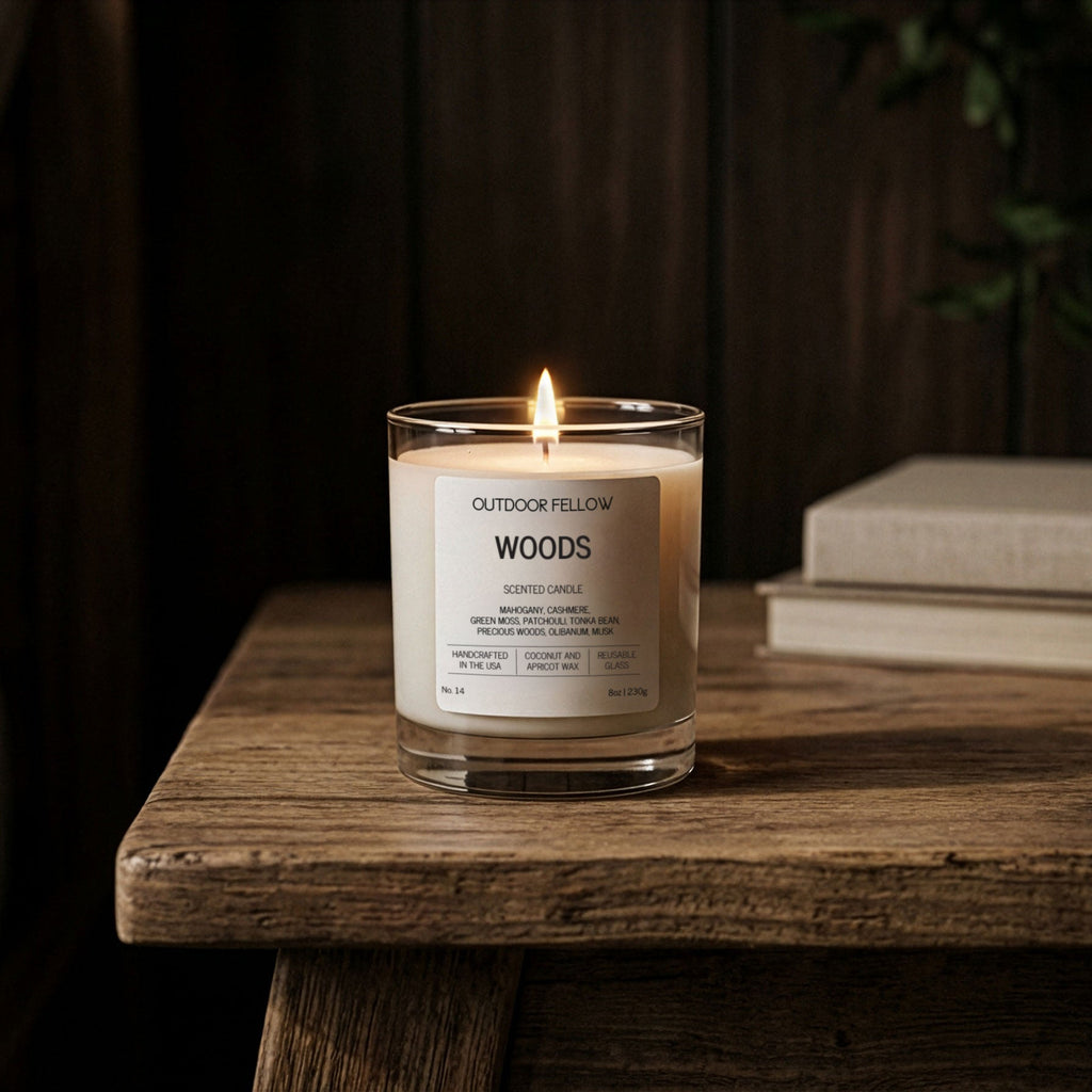 Candle labeled 'Woods' by Outdoor Fellow on a wooden surface with a dark background