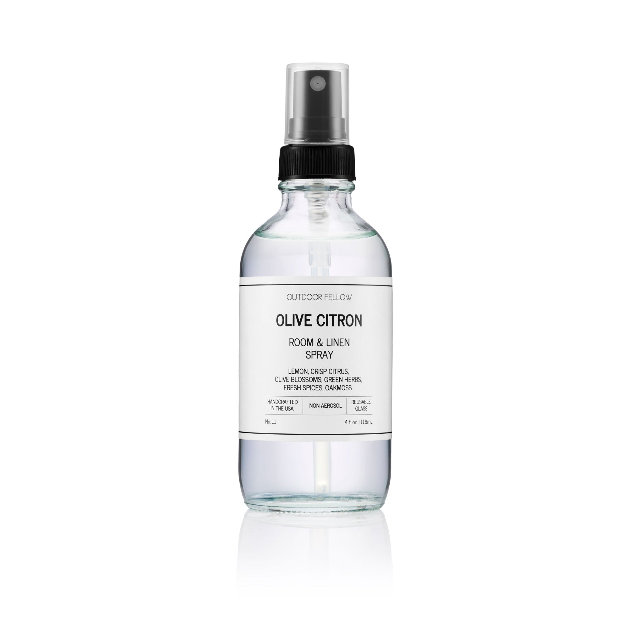 Clear glass spray bottle labeled Outdoor Fellow Olive Citron Room & Linen Spray with black spray top.