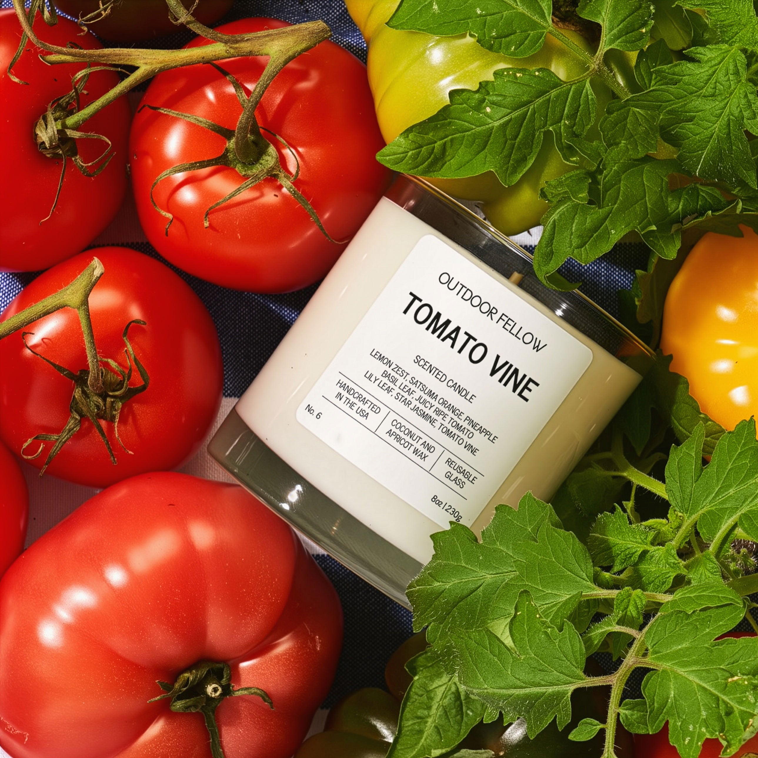 Candle labeled 'Tomato Vine' surrounded by fresh tomatoes and green leaves