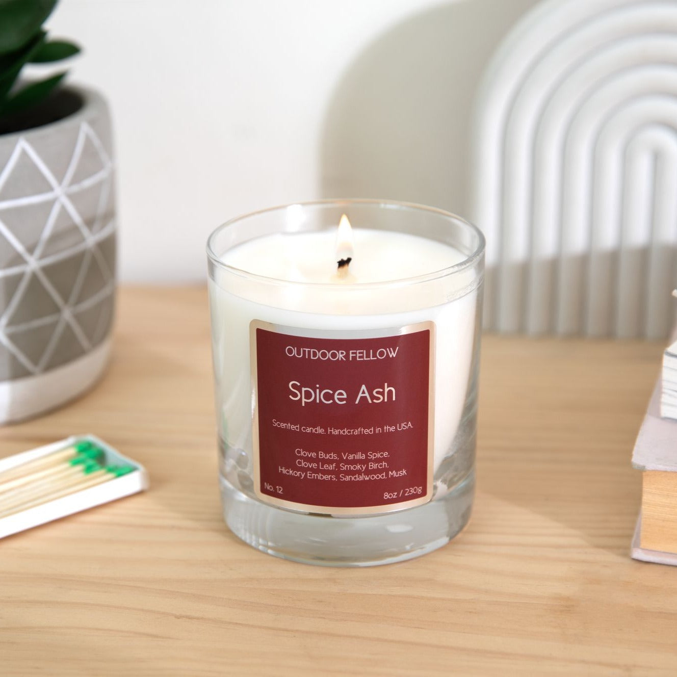 Spice Ash scented candle on wooden table with a book of matches