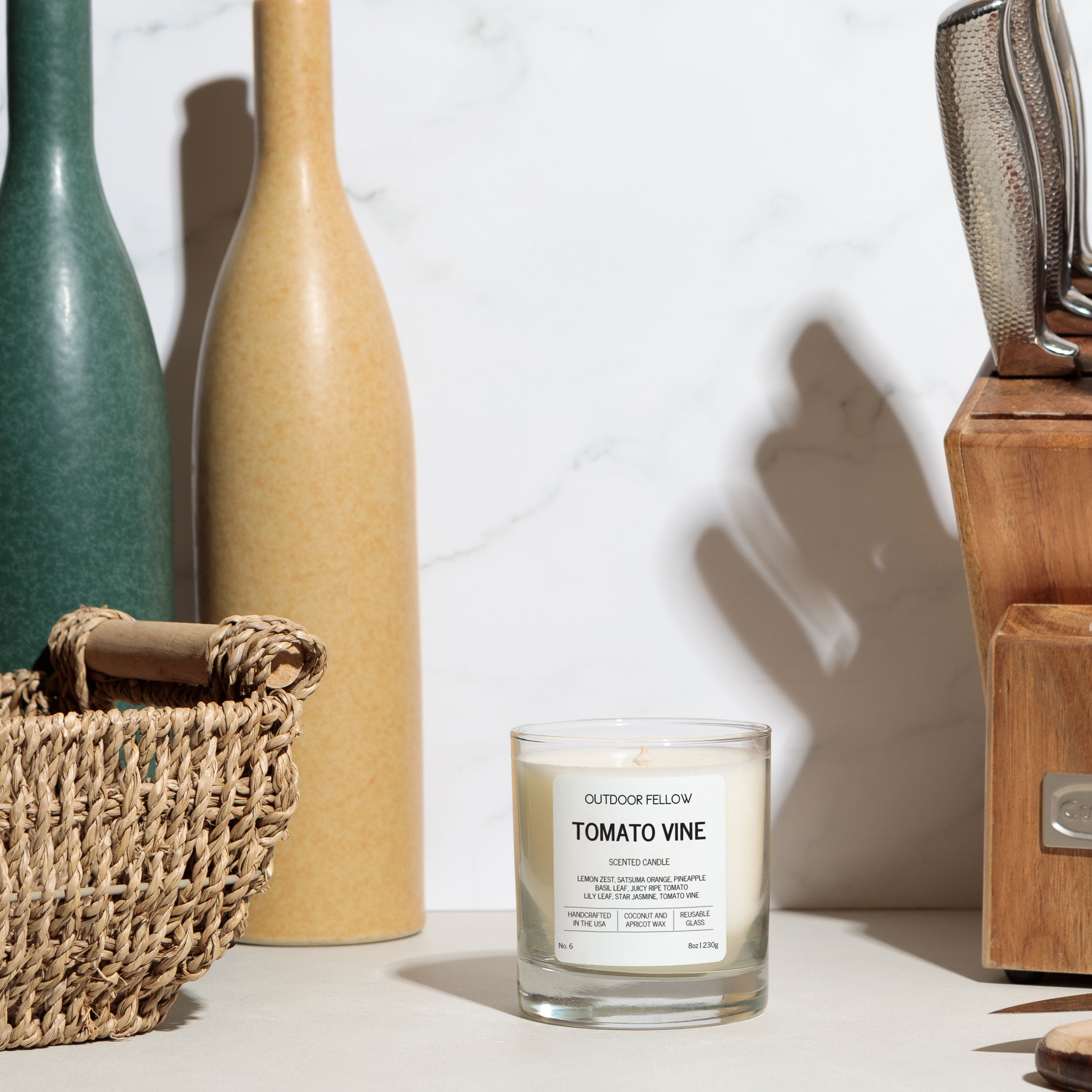 Candle labeled 'Tomato Vine' with decorative items including bottles and a basket on a light background