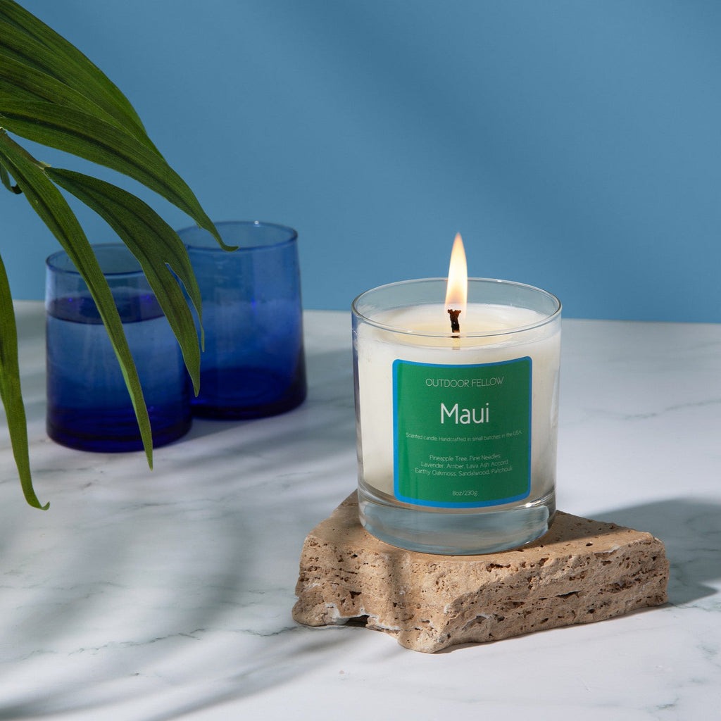 Maui scented candle on stone with blue cups in the background and a palm in the foreground