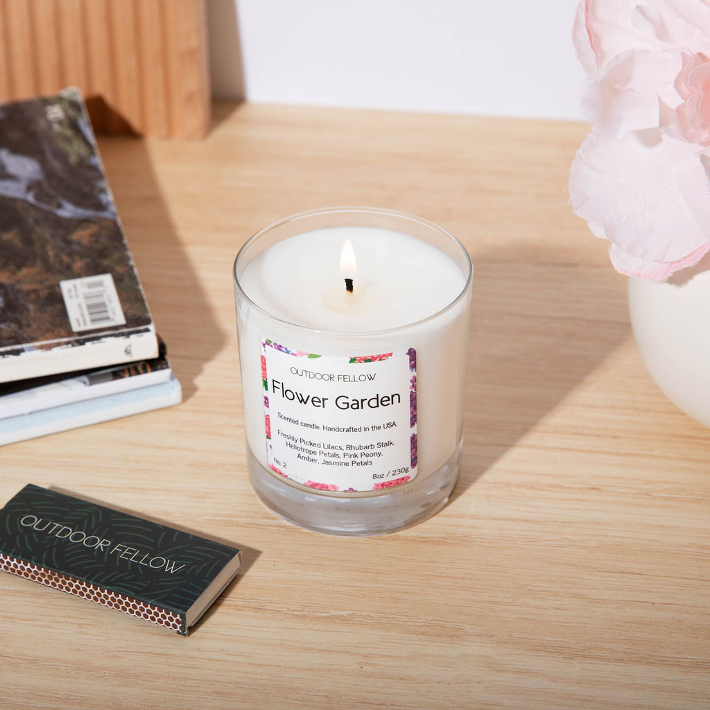 A lit Flower Garden scented candle on a table next to matches