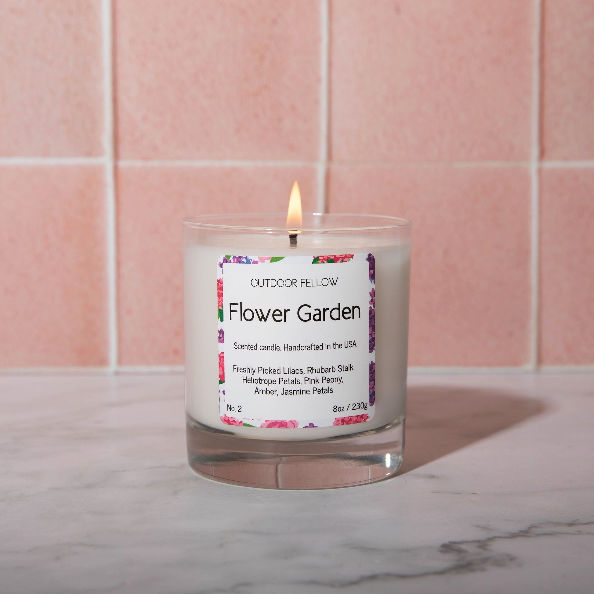 A lit Flower Garden scented candle on a marble surface with a pink tile background