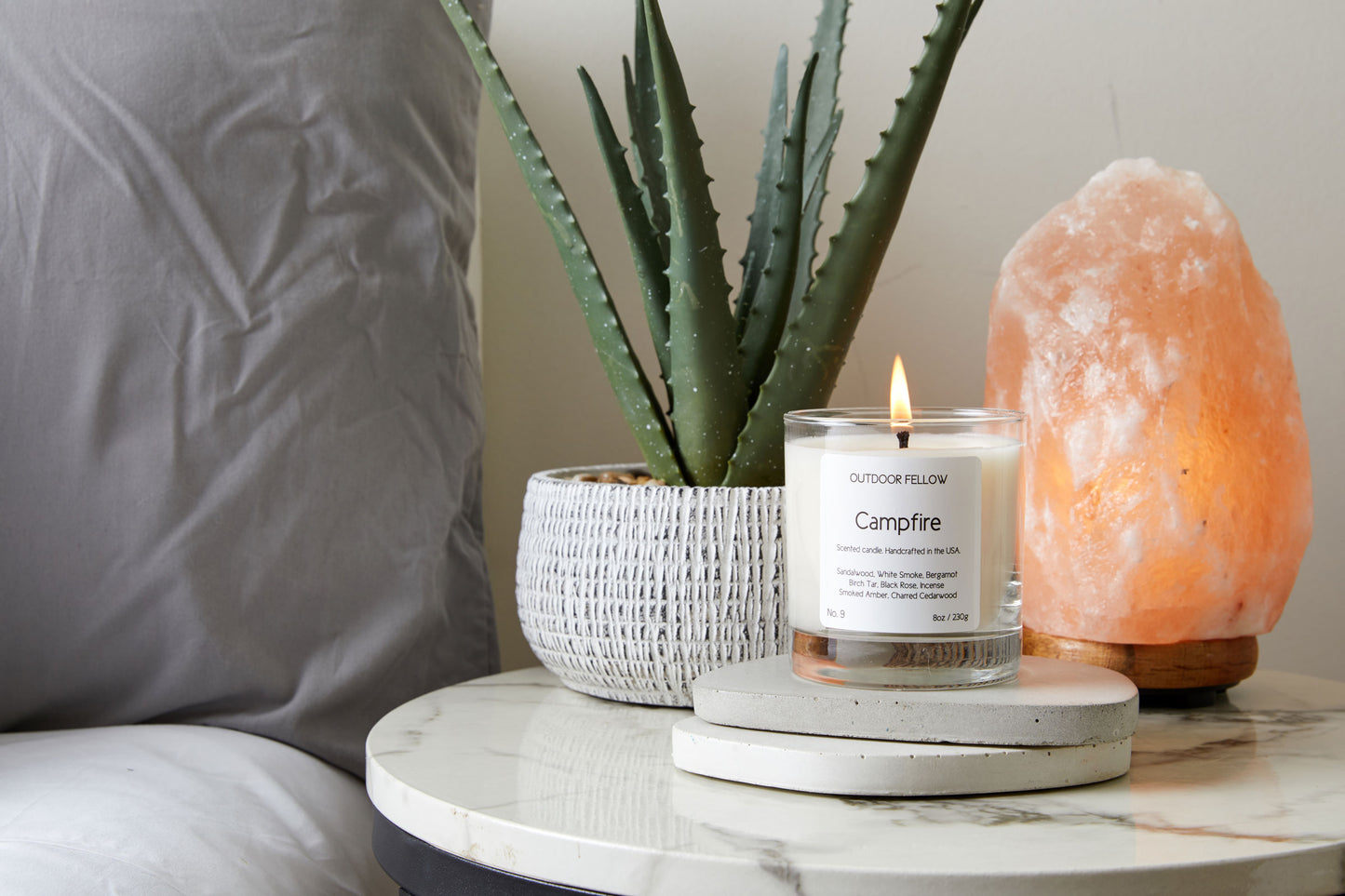 Campfire candle on nightstand next to aloe plant and rock salt lamp