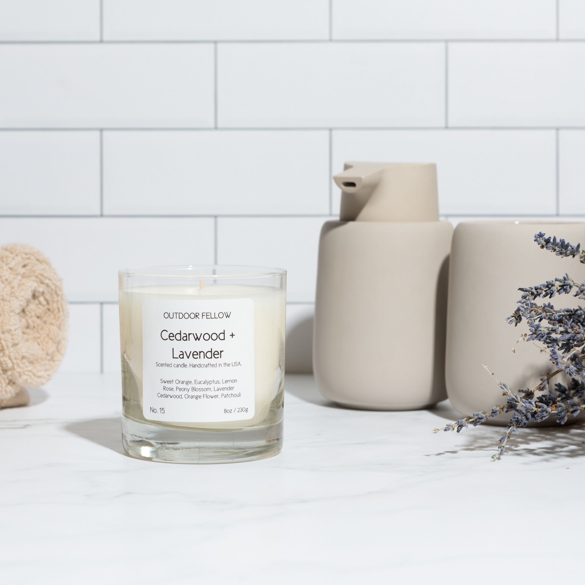Cedarwood and Lavender scented candle next to clay soap dispenser and sprigs of dried lavender