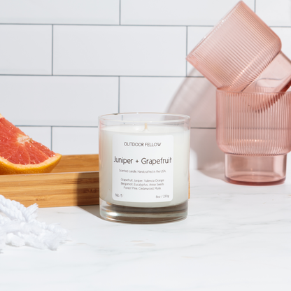Juniper and Grapefruit scented candle next to sliced grapefruit and pink tinted cups