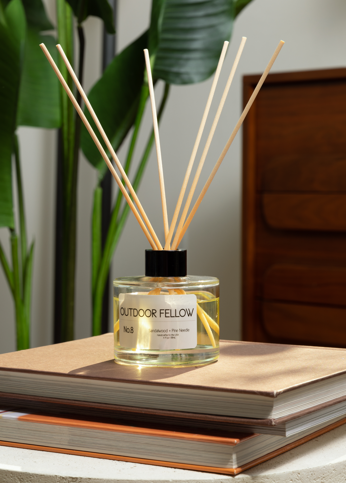 No.8 Sandalwood + Pine Needle reed diffuser on a stack of books in a living room