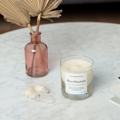 Rosa Moschata scented candle on marble coffee table next to a pink transparent vase and decorative objectss